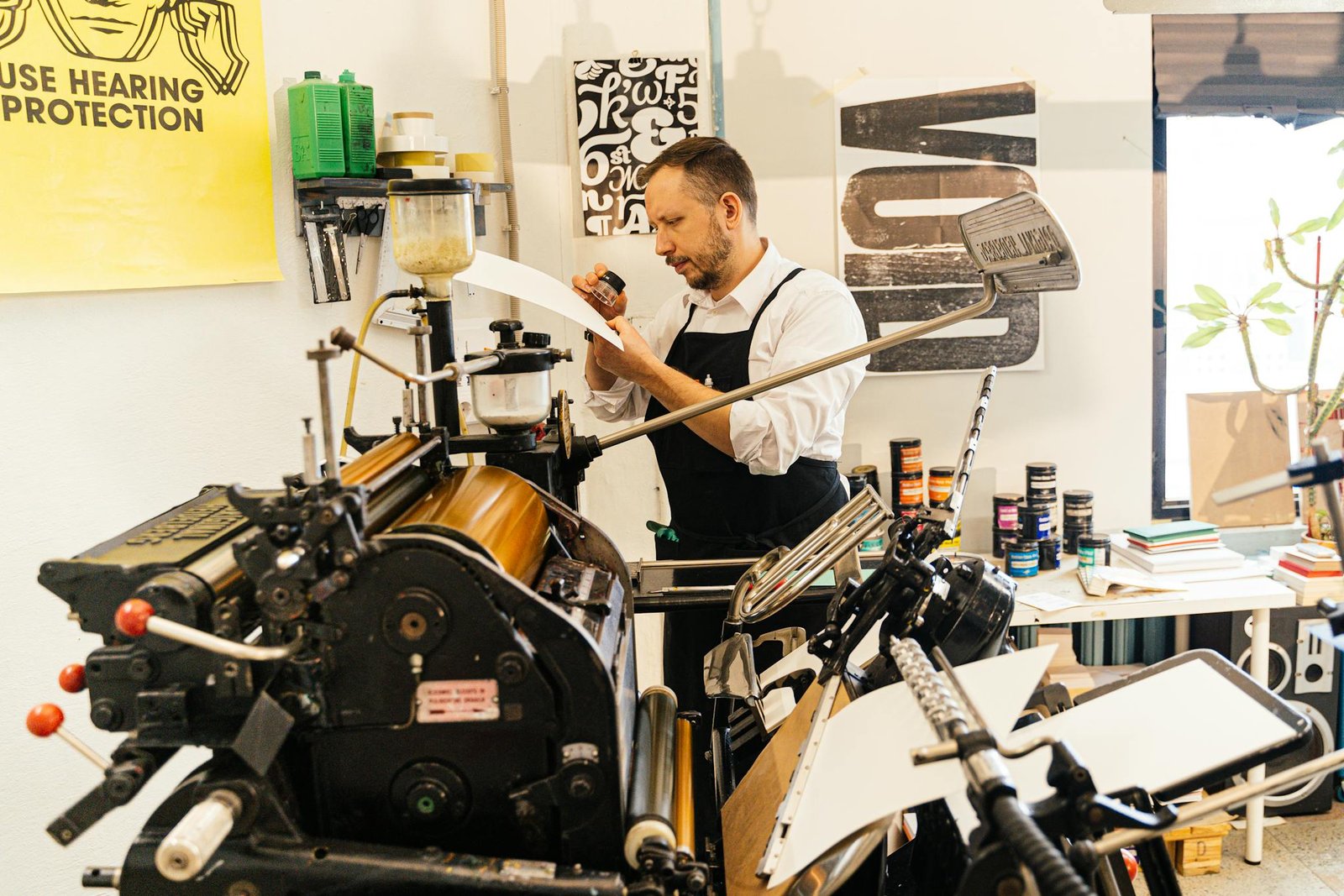Man in apron working with vintage printing press in workshop setting, emphasizing craftsmanship.